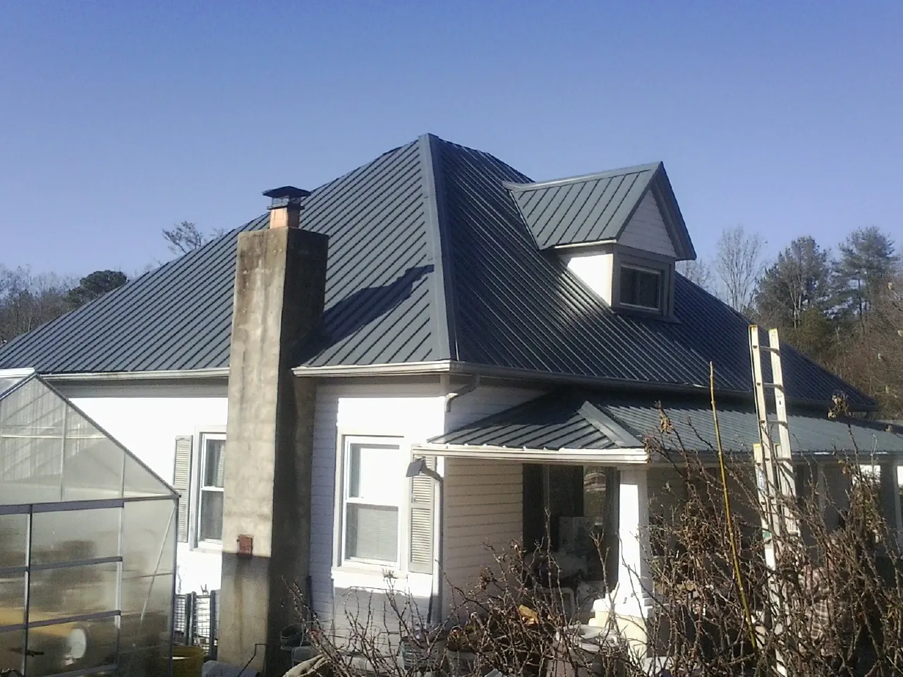 Dark blue standing seam metal roof on a white farmhouse with dormer — Slate & Tile Roof Repair by Roofing Brothers in Delta City