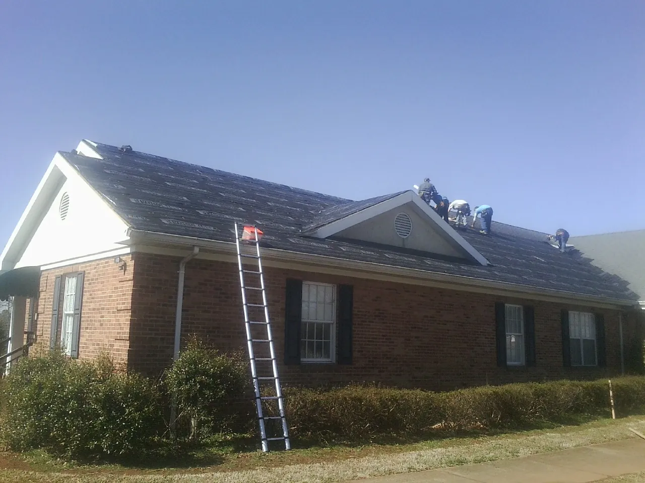 Crew tearing shingles off a brick ranch roof with a ladder set — Emergency Roof Repair work by our crew in Delta City