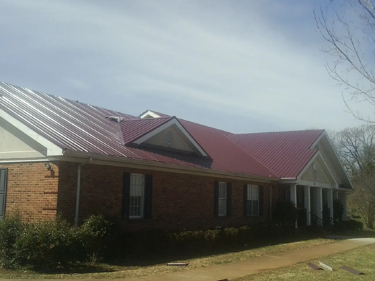 Red metal roof with gabled entries on a long brick building, from a Hail Damage Roof Repair job in Delta City