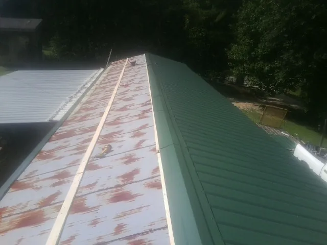 Old rusted panels beside newly installed green metal roofing — Wind Damage Roof Repair by Roofing Brothers in Delta City