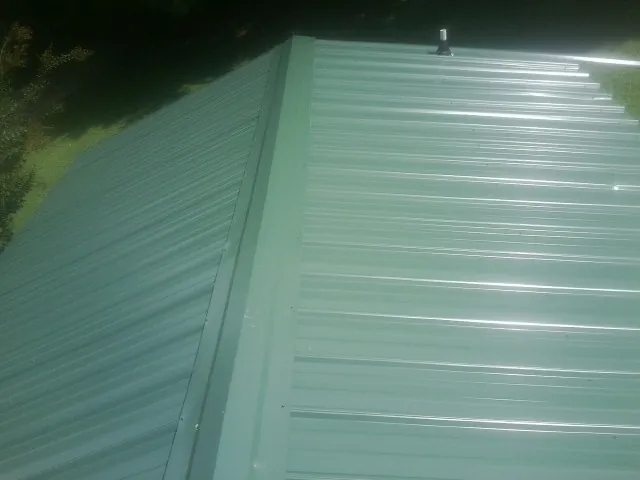 New green metal panels meeting at the ridge of a roof — Flat Roof Repair work by our crew in Delta City