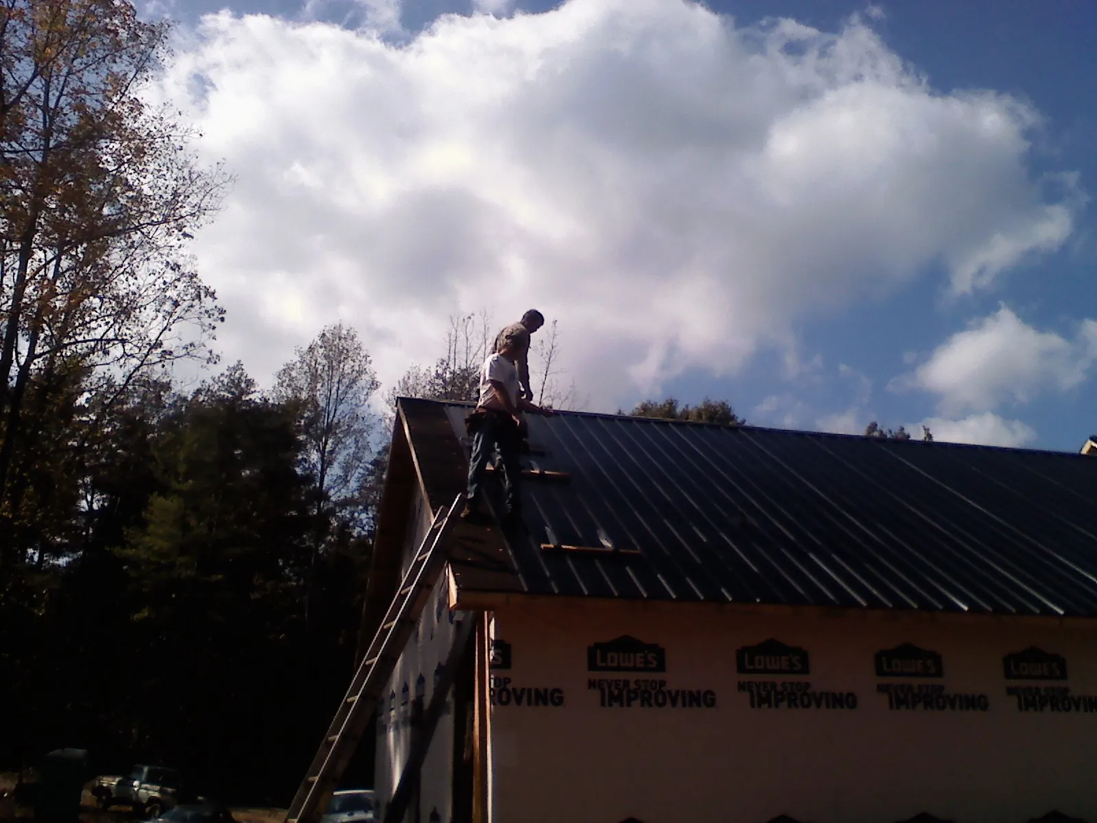 Roofer fastening dark metal panels high against a cloudy sky, from a Roof Inspection job in Delta City