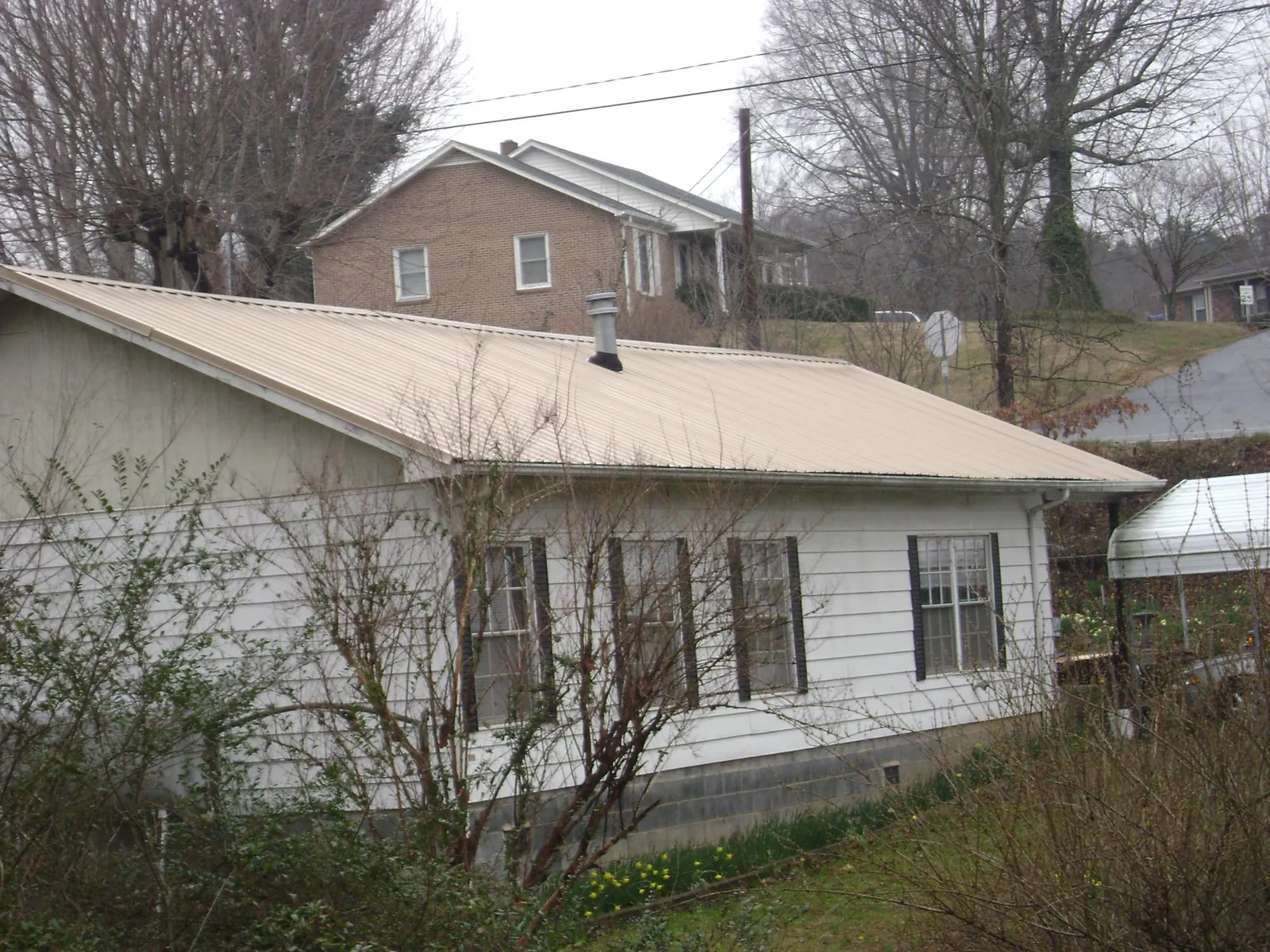 Tan metal roof on a white sided house set into a hillside — Commercial Roofing by Roofing Brothers in Delta City