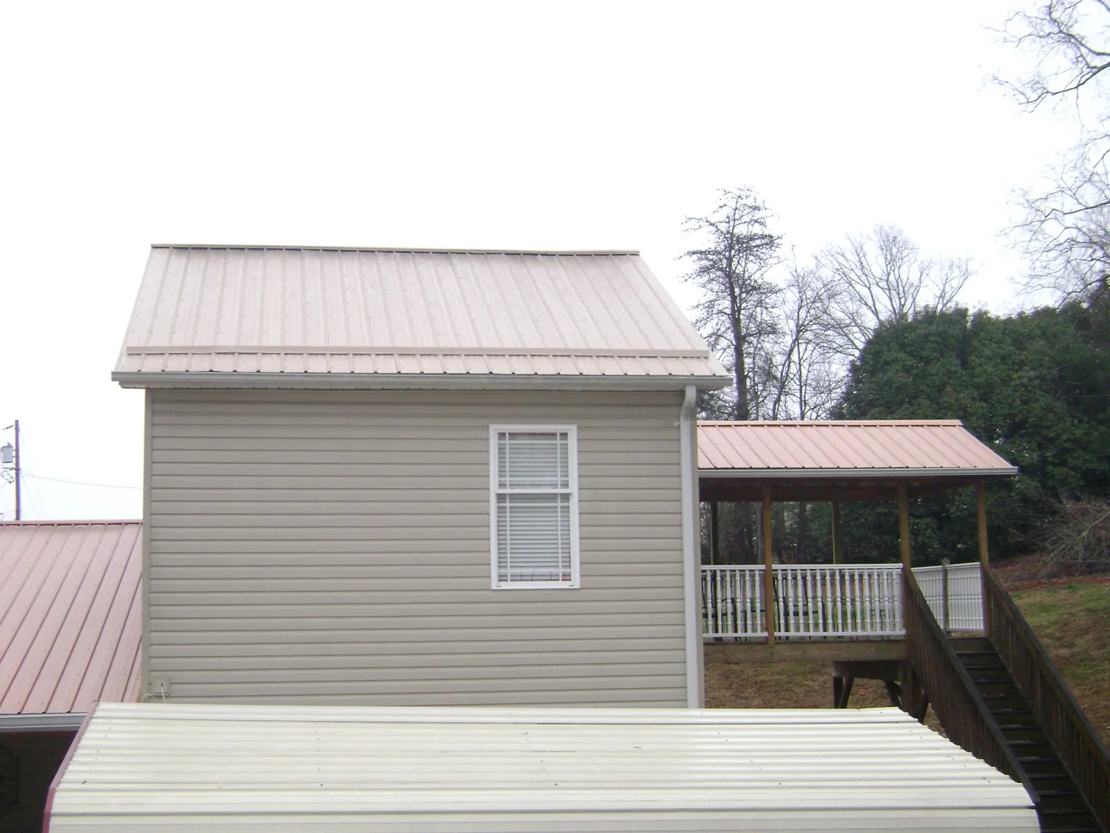 Tan metal roofs on a two story addition and attached porch, from a Roof Replacement job in Delta City